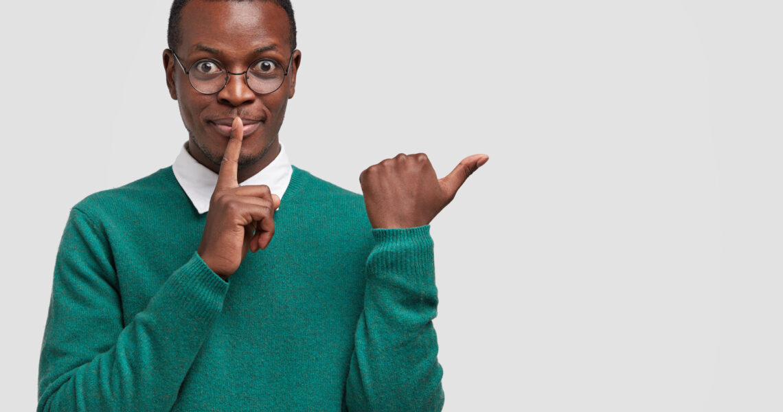 Business man holding a finger to his lips and pointing with his other hand