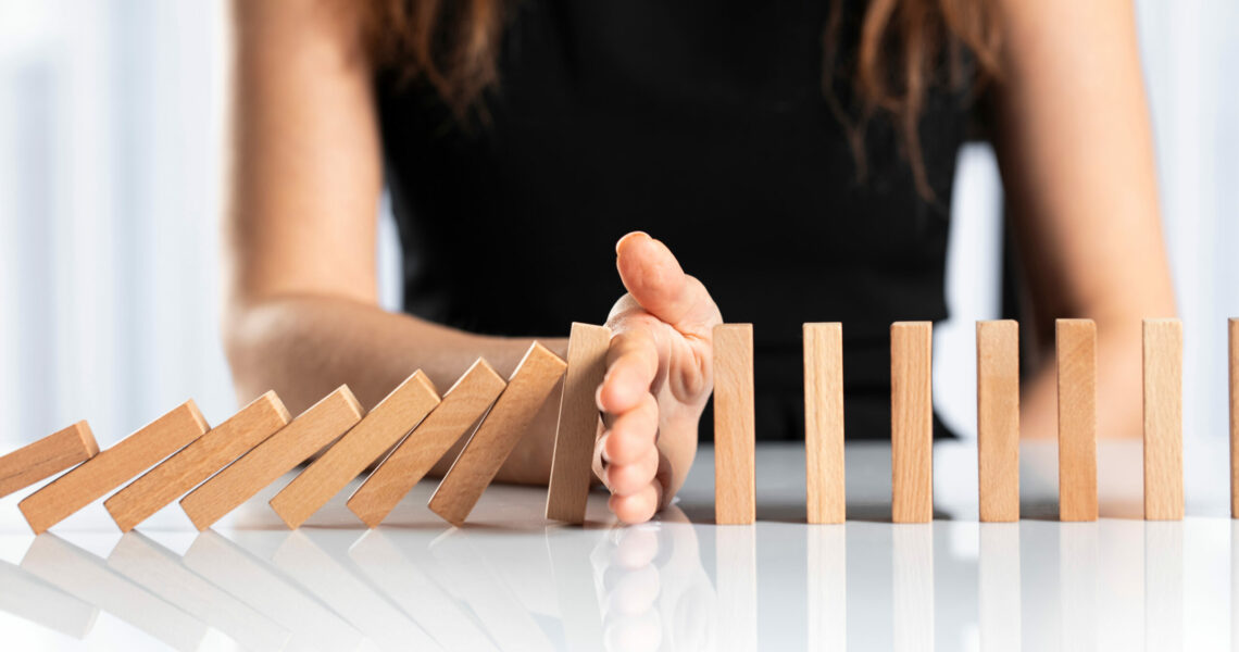 Woman sitting at desk placing her hand between a row of dominos and stopping it from falling