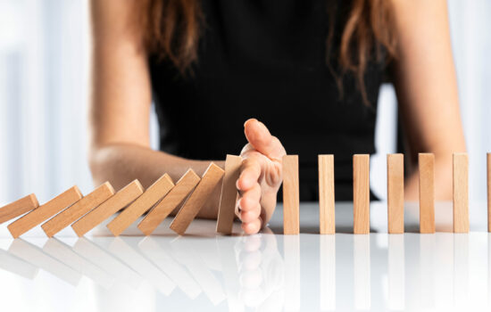 Woman sitting at desk placing her hand between a row of dominos and stopping it from falling