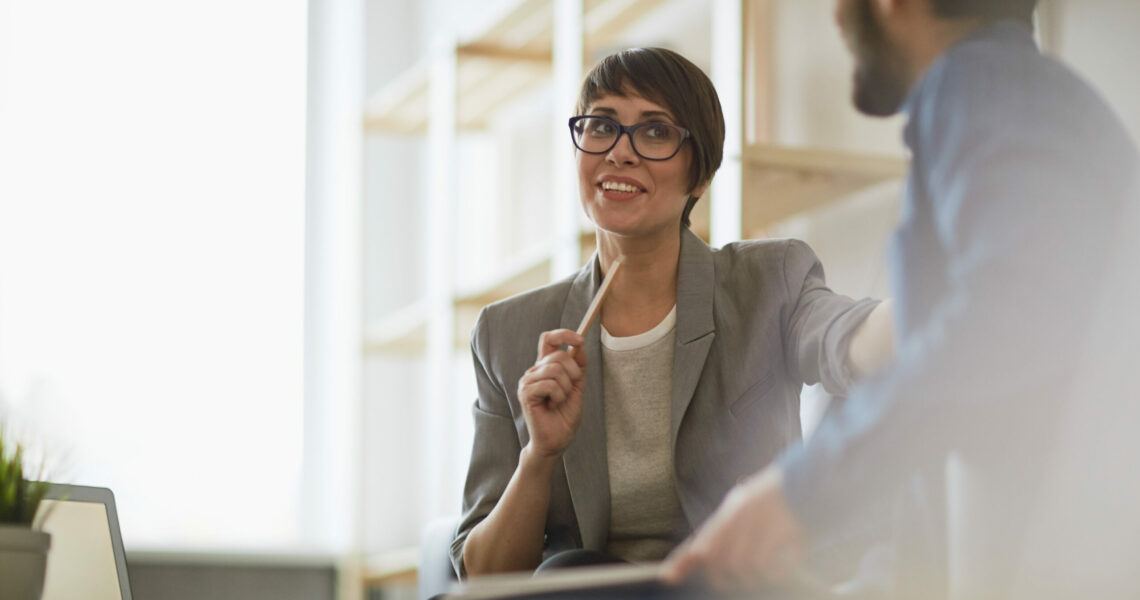 Smiling business woman talks to her colleague stretching one arm out to him