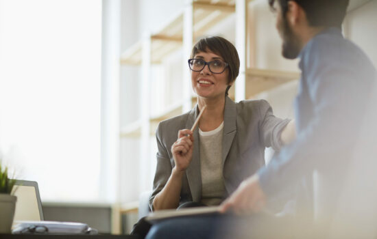 Smiling business woman talks to her colleague stretching one arm out to him