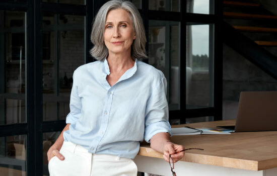 Confident woman with grey hair in a business shirt is looking directly at the camera