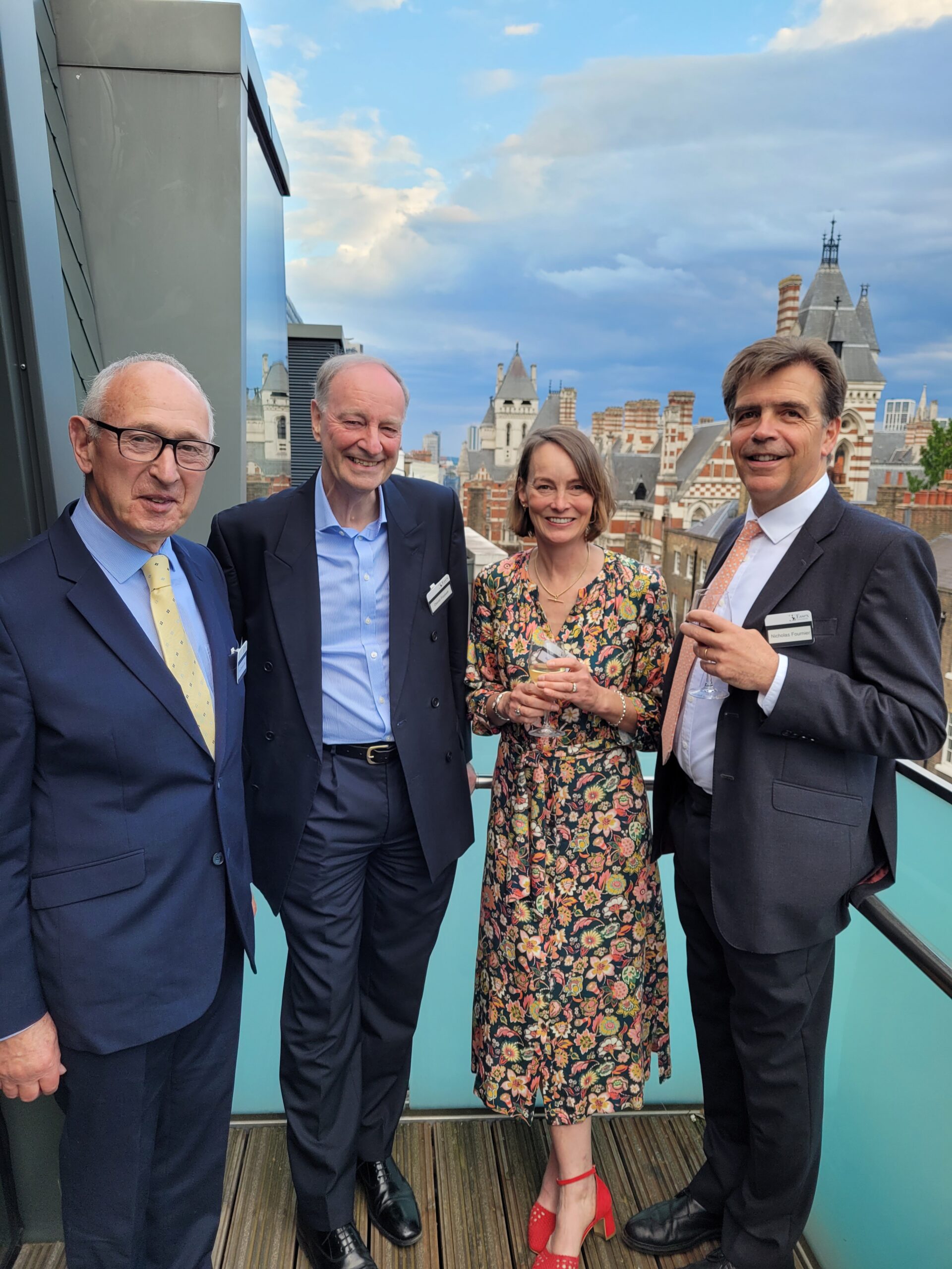 From left to right Tom Thomas OBE, Sir David Foskett, Rebecca Clark and Nicolas Fournier standing together smiling into the camera on a balcony at an event