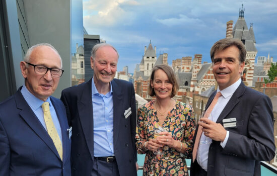 From left to right Tom Thomas OBE, Sir David Foskett, Rebecca Clark and Nicolas Fournier standing together smiling into the camera on a balcony at an event