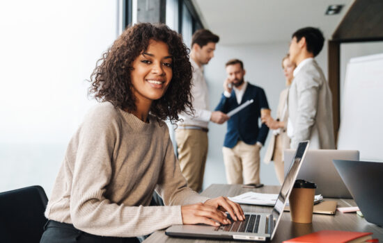 Young woman at laptop smiling at the camera group of people behind her