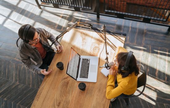 Man and woman sitting at a desk together recording a podcast seen from birdseye perspective