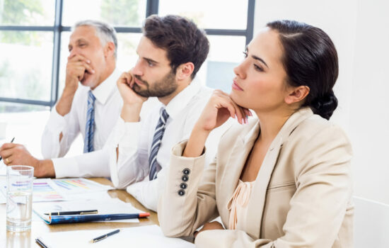 Three people at desk in a row looking critical and a little bored