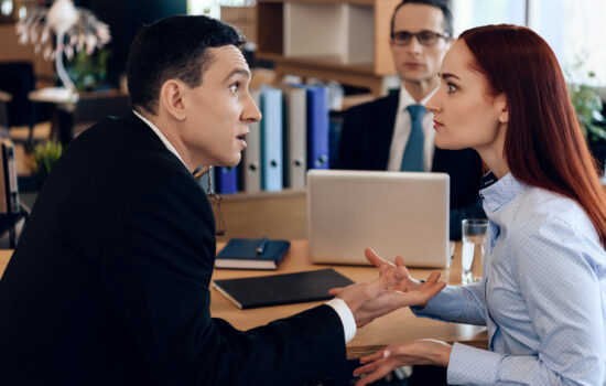 Couple arguing in an office, a third man sits behind them observing the conflict