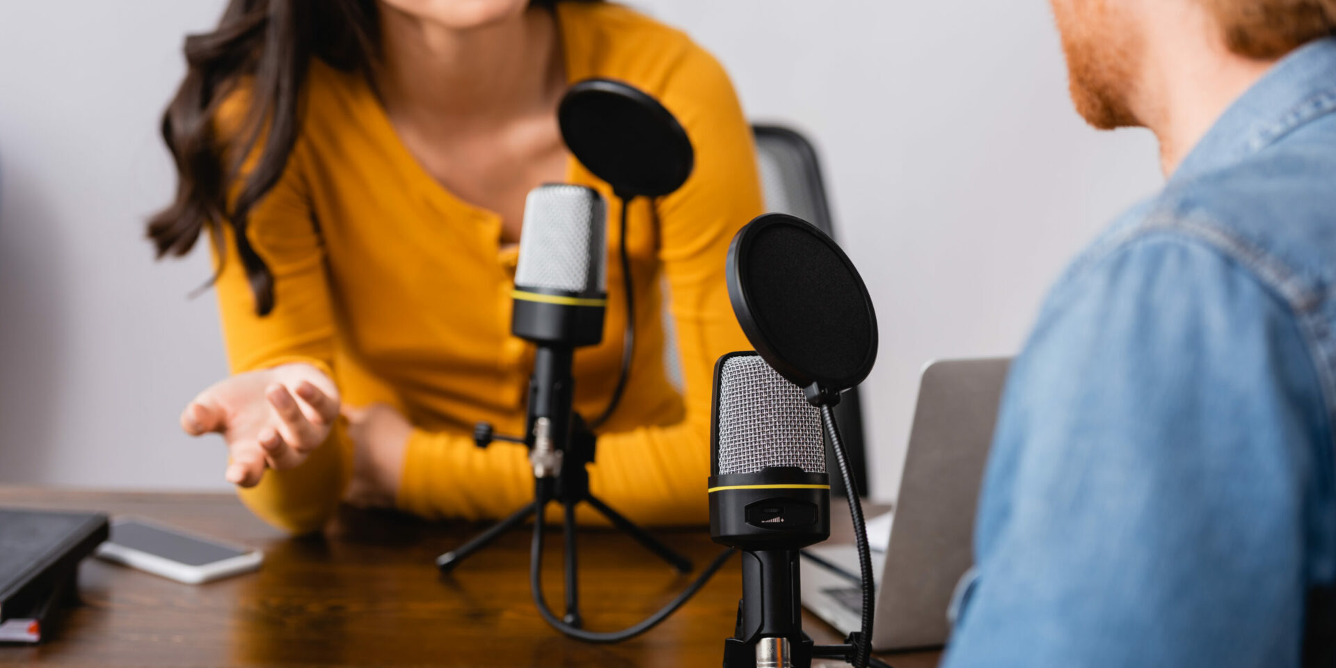 Man and woman recording a podcast sitting across from each other at a table