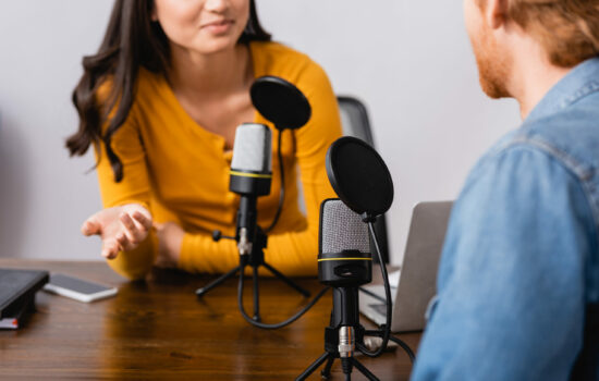 Man and woman recording a podcast sitting across from each other at a table